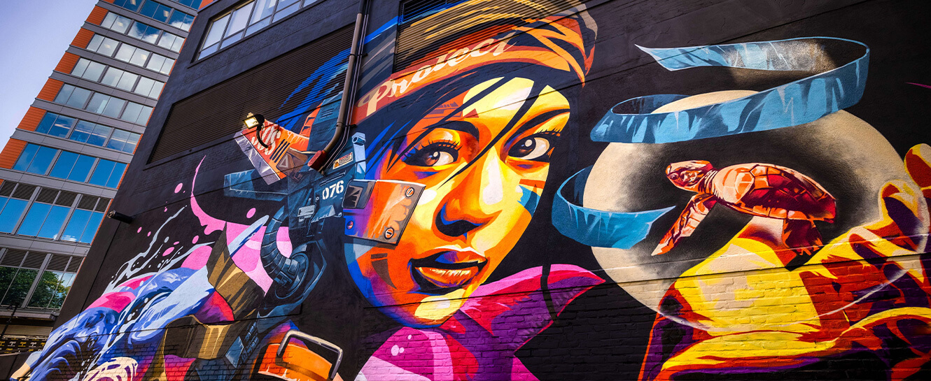 A spray-painted mural of a colorful woman and sea turtle, located on the side of a building in Boston.